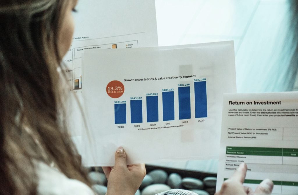 Photo of businesswoman from behind looking at papers with graph and return on investment table.